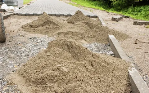 Kopce piasku czekają na ułożenie kostki brukowej. Trudno oszacować, ile piasku na m2 kostki, ale materiału jest sporo.