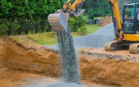 Koparka wysypuje tłuczeń do wykopu, tworząc fundament pod przyszłą drogę.