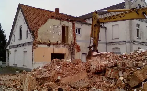 Rozbiórka budynku w granicy działki. Koparka Komatsu pracuje przy gruzach.