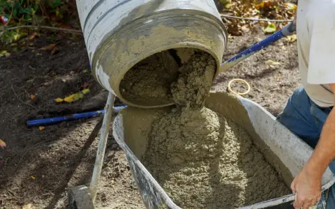 Betoniarka wylewa świeży beton do taczki. Właściwa ilość cementu na 1 m3 betonu jest kluczowa dla jego wytrzymałości.