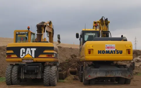 Dwie żółte koparko-ładowarki, CAT i Komatsu, stoją na placu budowy. Czy koparko ładowarka musi być zarejestrowana?