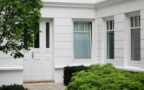 Boniowanie elewacji domu podkreśla jego klasyczny charakter. Białe drzwi i okna, otoczone zielenią, tworzą elegancką całość.