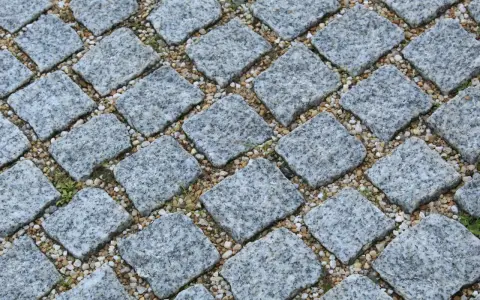 Szara kostka granitowa ułożona na podsypce. Widać, ile podsypki pod kostkę na m2 jest potrzebne do stabilnego ułożenia.