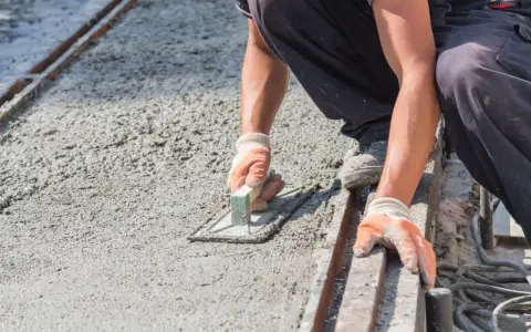 Pracownik w rękawicach wygładza świeży beton kielnią. To kluczowy etap, jak zrobić suchy beton, by był równy i trwały.