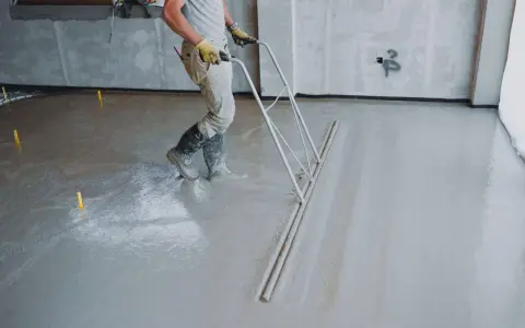 Pracownik wykonuje wylewkę betonową, wyrównując ją zacieraczką. Sprawdź wylewka betonowa cena za m2 robocizny bez materiału.