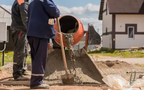 Dwóch budowlańców miesza beton. Zastanawiamy się, ile łopat żwiru na worek cementu, by uzyskać idealną konsystencję.