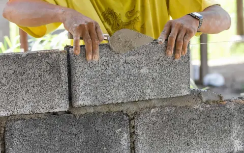 Budowniczy układa kostkę fundamentową na zaprawie.
