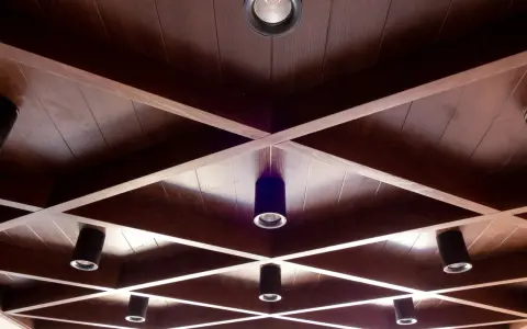 Drewniane, kratownicowe **stare kasetony na suficie** z wbudowanymi reflektorami tworzą geometryczny wzór.