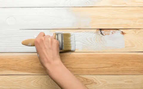 Ręka maluje białą farbą drewnianą boazerię, odświeżając jej wygląd.