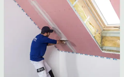 Fachowiec wykonuje gipsowanie ścian z płyty gipsowo-kartonowej, nakładając masę szpachlową na połączenie płyt.