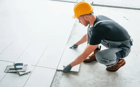 Fachowiec układa płytki na balkonie. Dowiedz się, ile kosztuje położenie płytek na balkonie i jakie materiały są potrzebne.