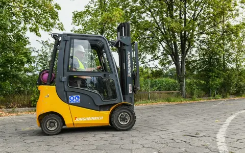 Operator w kasku i kamizelce prowadzi wózek widłowy Jungheinrich. Zastanawiasz się, ile kosztuje uprawnienia na wózek widłowy?