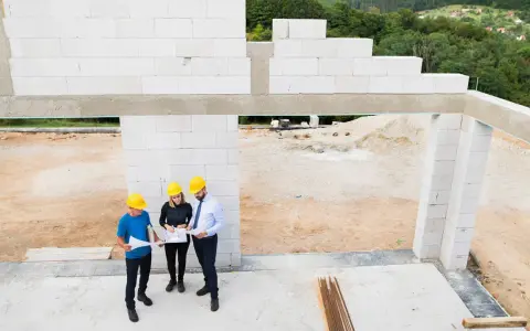 Architekci omawiają projekt domu z bloczków silikatowych. Budowa w toku, w tle zielone wzgórza.