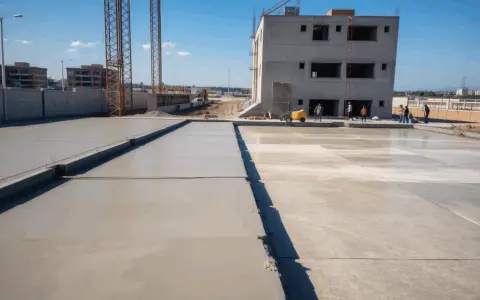 Plac budowy z nowo wylanym betonem, budynkiem w tle i dźwigami. Zastanawiasz się, ile betonu z worka cementu?