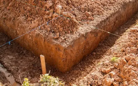 Wykonano wykopy pod fundamenty. Widać głębokie rowy w ziemi, wyznaczone sznurkami.
