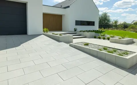 Nowoczesne wzory kostki brukowej przed domem tworzą schludny podjazd i ścieżki, otoczone geometrycznymi rabatami.