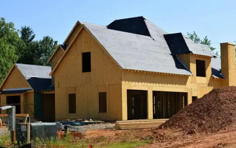 Dom w budowie z widocznym deskowaniem dachu. Widać konstrukcję ścian z płyt OSB i rozpoczęte prace nad pokryciem dachu.
