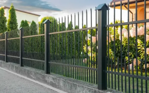 Betonowy murek jako alternatywa dla podmurówki pod ogrodzenie. Czarny metalowy płot z ostrymi zakończeniami.