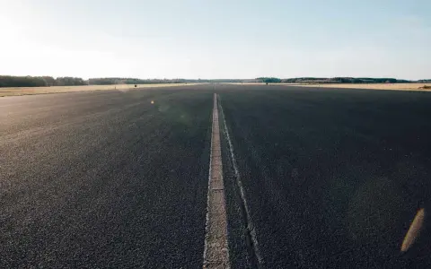 Asfaltowa droga z linią pośrodku, otoczona polami i lasem.