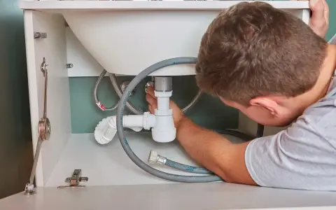 Hydraulik naprawia syfon pod zlewem. Zastanawiasz się, ile kosztuje hydraulik?