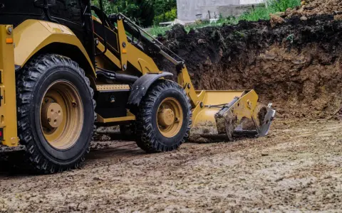 Koparka pracuje nad tym, jak wyrównać działkę, usuwając ziemię z wykopu.