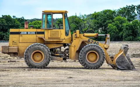 Żółta koparko-ładowarka John Deere 624G gotowa do pracy, wymaga odpowiednich uprawnień do obsługi.