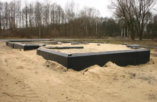 Fundament domu w piasku, z czarną izolacją przeciwwilgociową wokół.