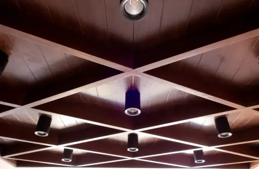 Drewniane, kratownicowe **stare kasetony na suficie** z wbudowanymi reflektorami tworzą geometryczny wzór.