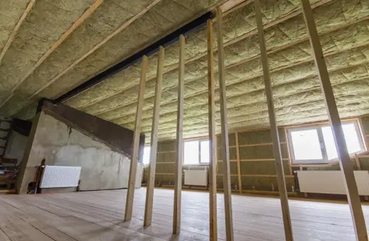 Ocieplenie stropu betonowego wełną mineralną. Widać drewnianą konstrukcję, okna i grzejniki.