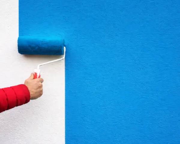 Malowanie ściany na niebiesko wałkiem. Ta farba wygłuszająca ściany nada pomieszczeniu nowy wygląd i poprawi akustykę.