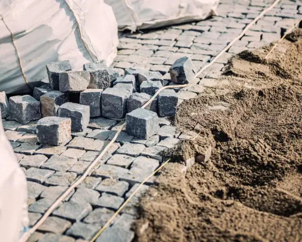 Kupa kostki brukowej i piasku, gotowe do ułożenia. Widać worki z materiałem i przygotowany podkład, czyli ile podsypki pod kostkę potrzeba.