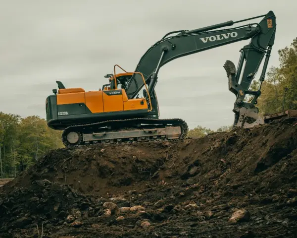 Pomarańczowo-czarna koparka Volvo EC220DL pracuje na budowie. Operator koparki gąsienicowej zarabia dobrze, wykonując ciężką pracę.