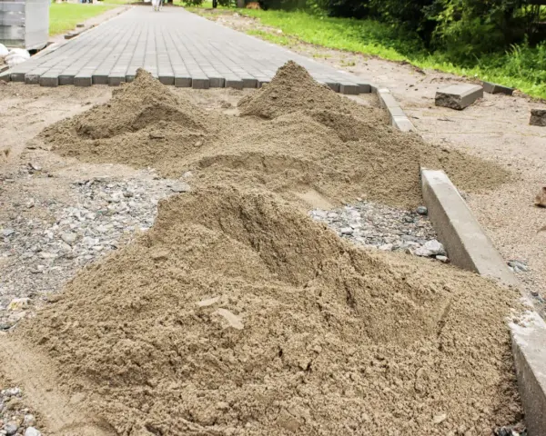 Kopce piasku czekają na ułożenie kostki brukowej. Trudno oszacować, ile piasku na m2 kostki, ale materiału jest sporo.