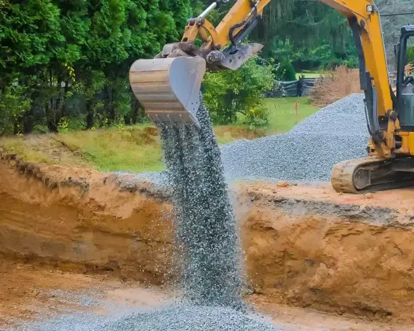 Koparka wysypuje tłuczeń do wykopu, tworząc fundament pod przyszłą drogę.