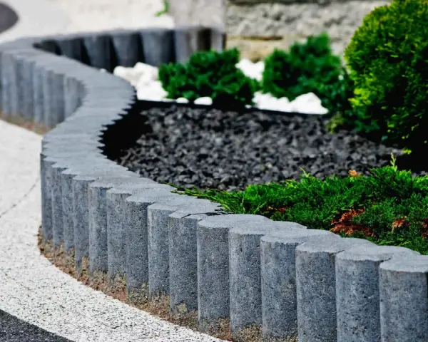 Obrzeże z kostki granitowej tworzy falistą linię, oddzielając ścieżkę od zadbanej rabaty z iglakami i kamieniami.