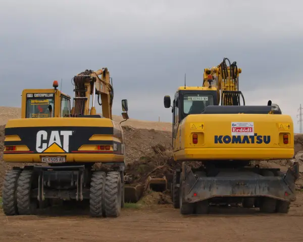 Dwie żółte koparko-ładowarki, CAT i Komatsu, stoją na placu budowy. Czy koparko ładowarka musi być zarejestrowana?