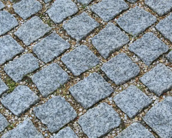 Szara kostka granitowa ułożona na podsypce. Widać, ile podsypki pod kostkę na m2 jest potrzebne do stabilnego ułożenia.