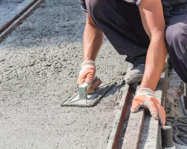 Pracownik w rękawicach wygładza świeży beton kielnią. To kluczowy etap, jak zrobić suchy beton, by był równy i trwały.