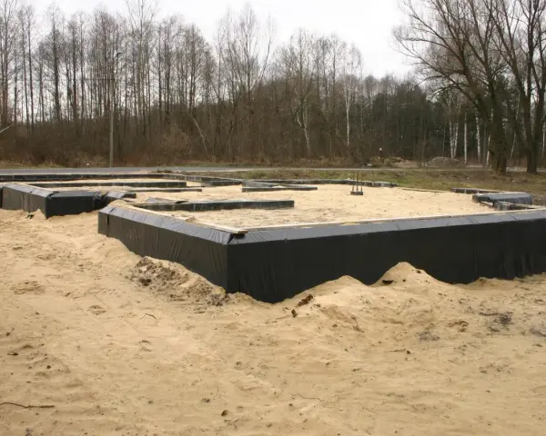 Fundament domu w piasku, z czarną izolacją przeciwwilgociową wokół.