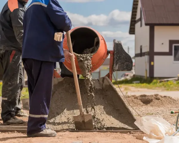 Dwóch budowlańców miesza beton. Zastanawiamy się, ile łopat żwiru na worek cementu, by uzyskać idealną konsystencję.
