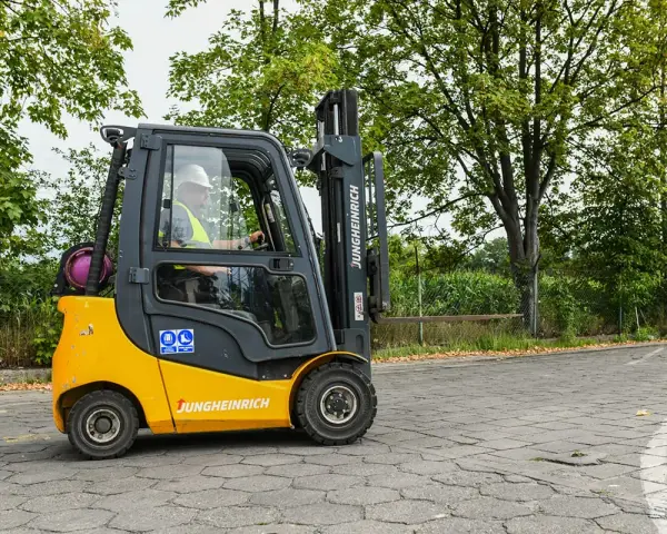 Operator w kasku i kamizelce prowadzi wózek widłowy Jungheinrich. Zastanawiasz się, ile kosztuje uprawnienia na wózek widłowy?