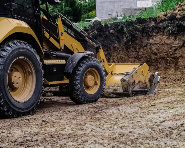 Koparka pracuje nad tym, jak wyrównać działkę, usuwając ziemię z wykopu.