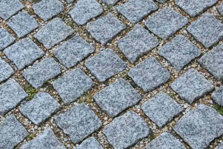 Szara kostka granitowa ułożona na podsypce. Widać, ile podsypki pod kostkę na m2 jest potrzebne do stabilnego ułożenia.