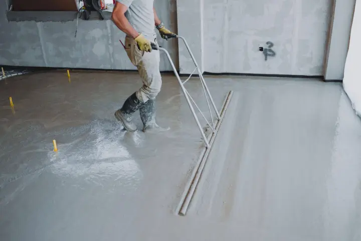 Pracownik wykonuje wylewkę betonową, wyrównując ją zacieraczką. Sprawdź wylewka betonowa cena za m2 robocizny bez materiału.