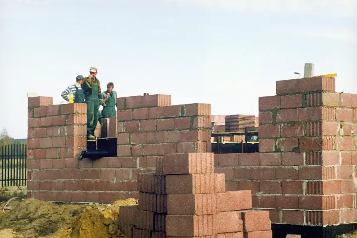 Budowa domu w toku. Brygada murarzy pracuje, a fundamenty muszą odstać, zanim ruszą dalsze prace.