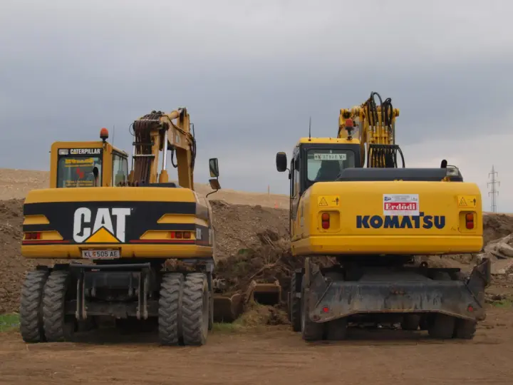 Dwie żółte koparko-ładowarki, CAT i Komatsu, stoją na placu budowy. Czy koparko ładowarka musi być zarejestrowana?