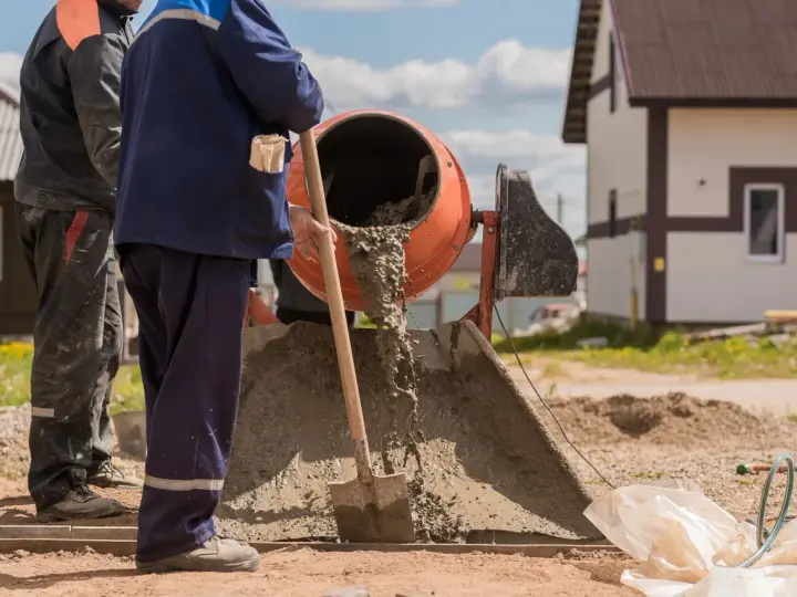 Dwóch budowlańców miesza beton. Zastanawiamy się, ile łopat żwiru na worek cementu, by uzyskać idealną konsystencję.