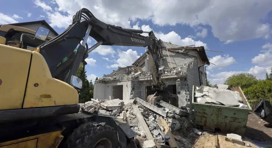 Koparka Volvo niszczy budynek. Trwa rozbiórka budynku, cena za m2 jest kluczowa przy planowaniu prac.