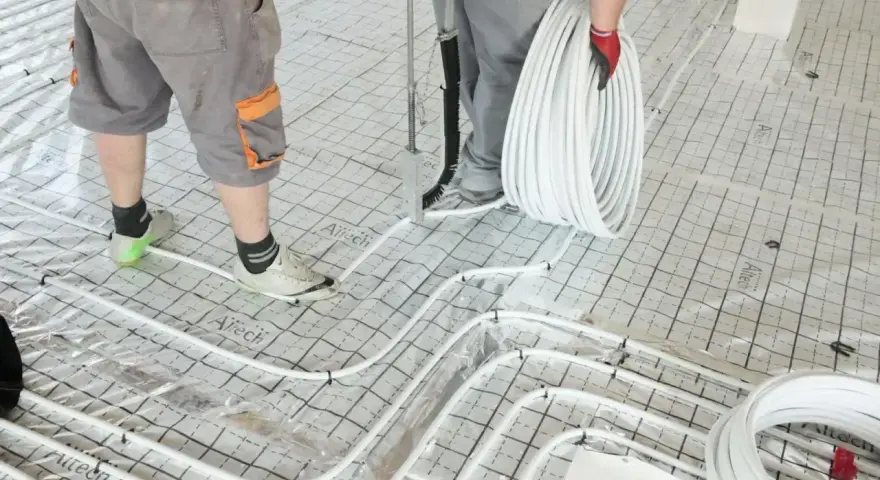 Pracownicy układają rury do ogrzewania podłogowego na siatce. Wkrótce powstanie tu szlichta, która zapewni komfort cieplny.
