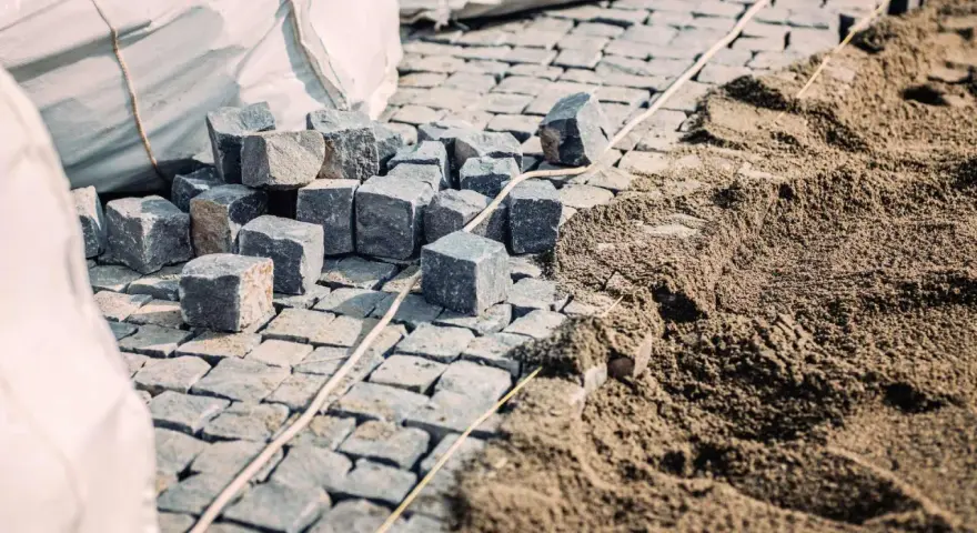 Kupa kostki brukowej i piasku, gotowe do ułożenia. Widać worki z materiałem i przygotowany podkład, czyli ile podsypki pod kostkę potrzeba.